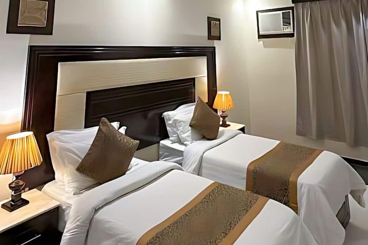 Habitación de hotel con dos camas, una mesita de noche con lámpara, un cuadro en la pared y una ventana con cortinas.