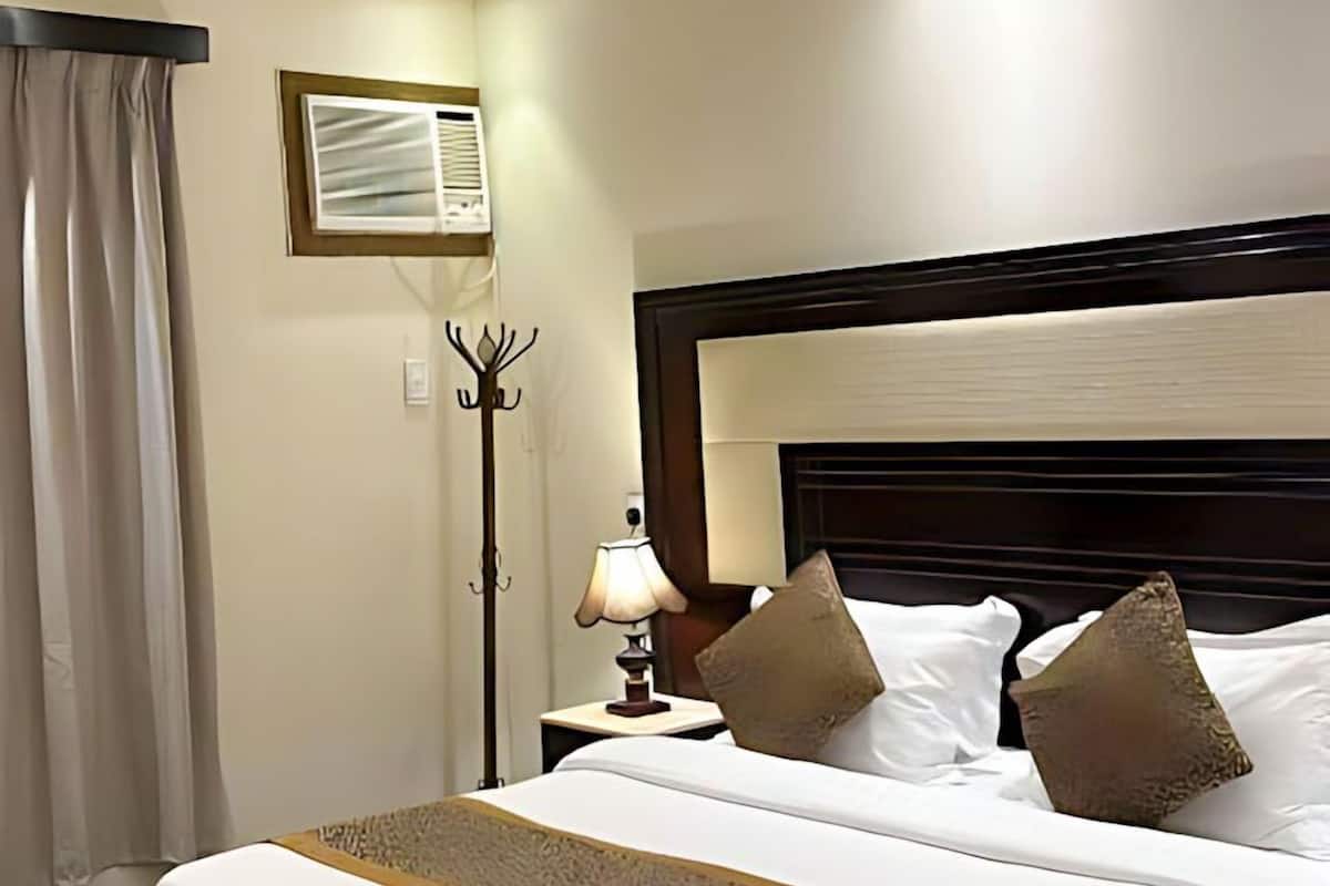 Habitación de hotel con una cama grande, una mesita de noche con lámpara, un perchero y una ventana con cortinas.