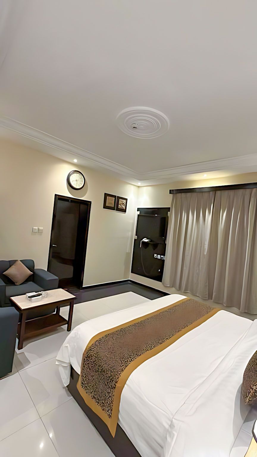 Ein Hotelzimmer mit Bett, einer Couch, einem kleinen Tisch, einer Tür und einem Duschbereich.