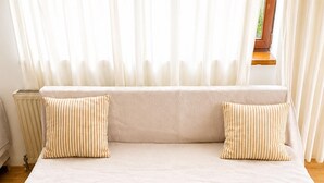 Un sofá cama con dos almohadas, un radiador y una ventana con cortinas.