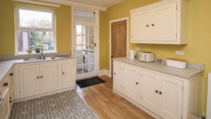 A kitchen with white cabinets, a wooden floor, a patterned rug, and a window with a view of the outside. - The Manse (Saltburn-by-the-Sea)
