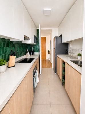 A modern kitchen with white cabinets, a green backsplash, and a stainless steel refrigerator.