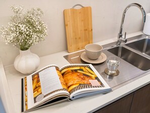A kitchen counter with a cookbook, a cutting board, a vase with flowers, and a glass of water.