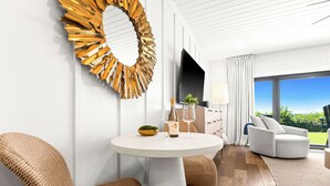 Ein modernes Wohnzimmer mit einem runden Tisch, Korbstühlen, einem großen Spiegel, einem Flachbildfernseher und Blick ins Freie.