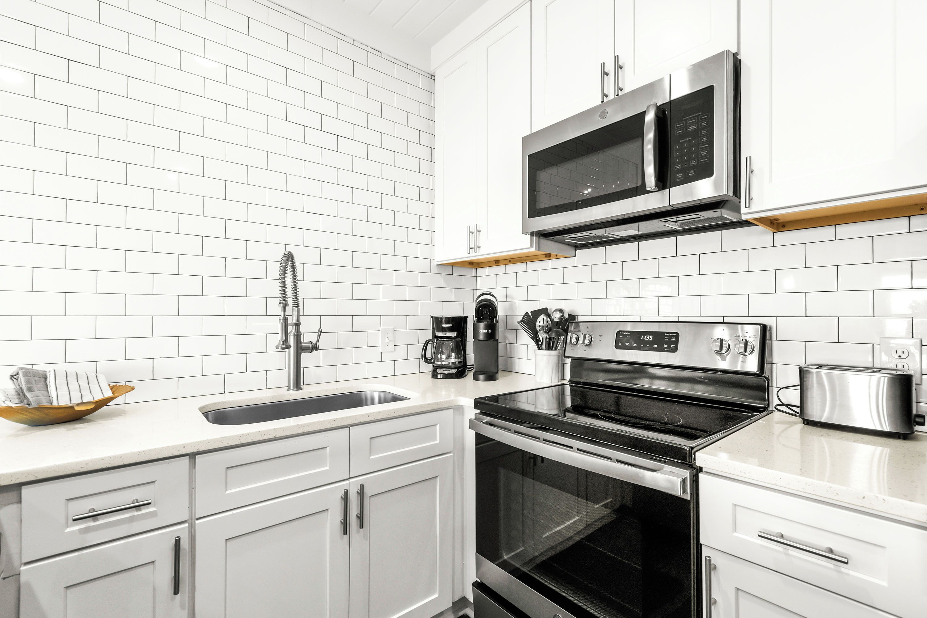 A modern kitchen with white cabinets, a stainless steel stove, a microwave, and a coffee maker.