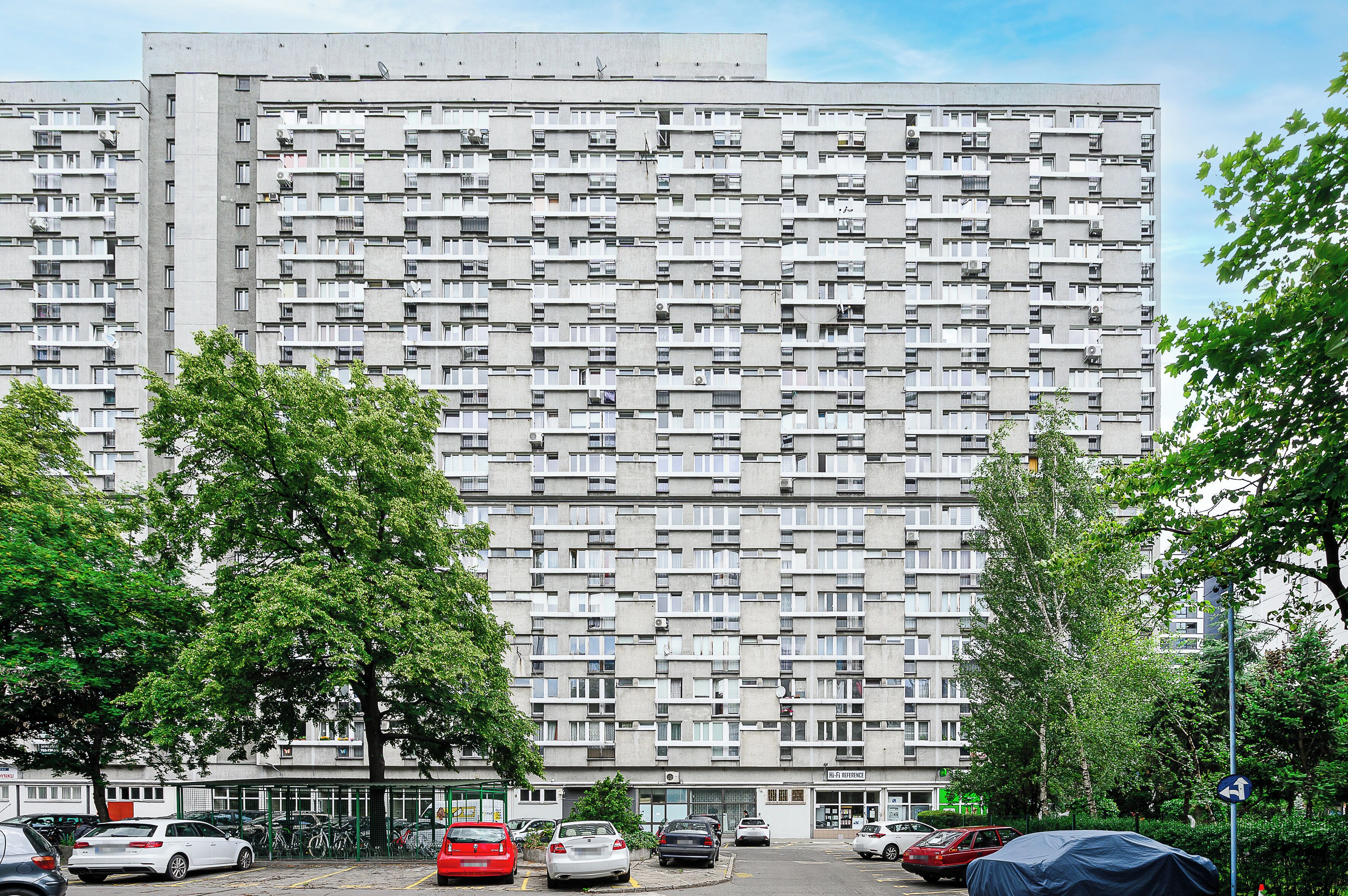 Um edifício residencial alto com várias varandas e uma área de estacionamento na frente.