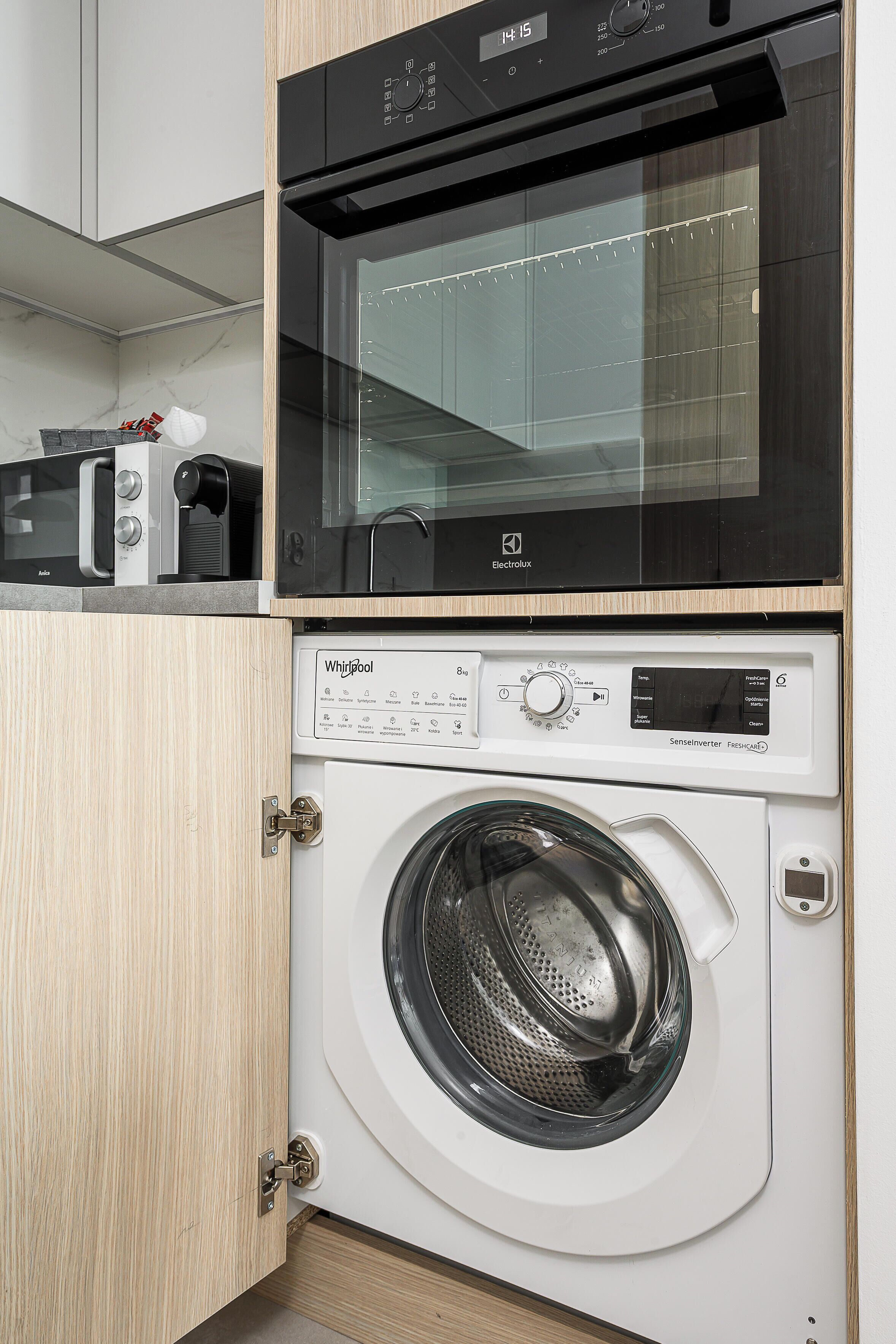 A compact kitchen with a microwave, toaster, and a black oven above a white washing machine.