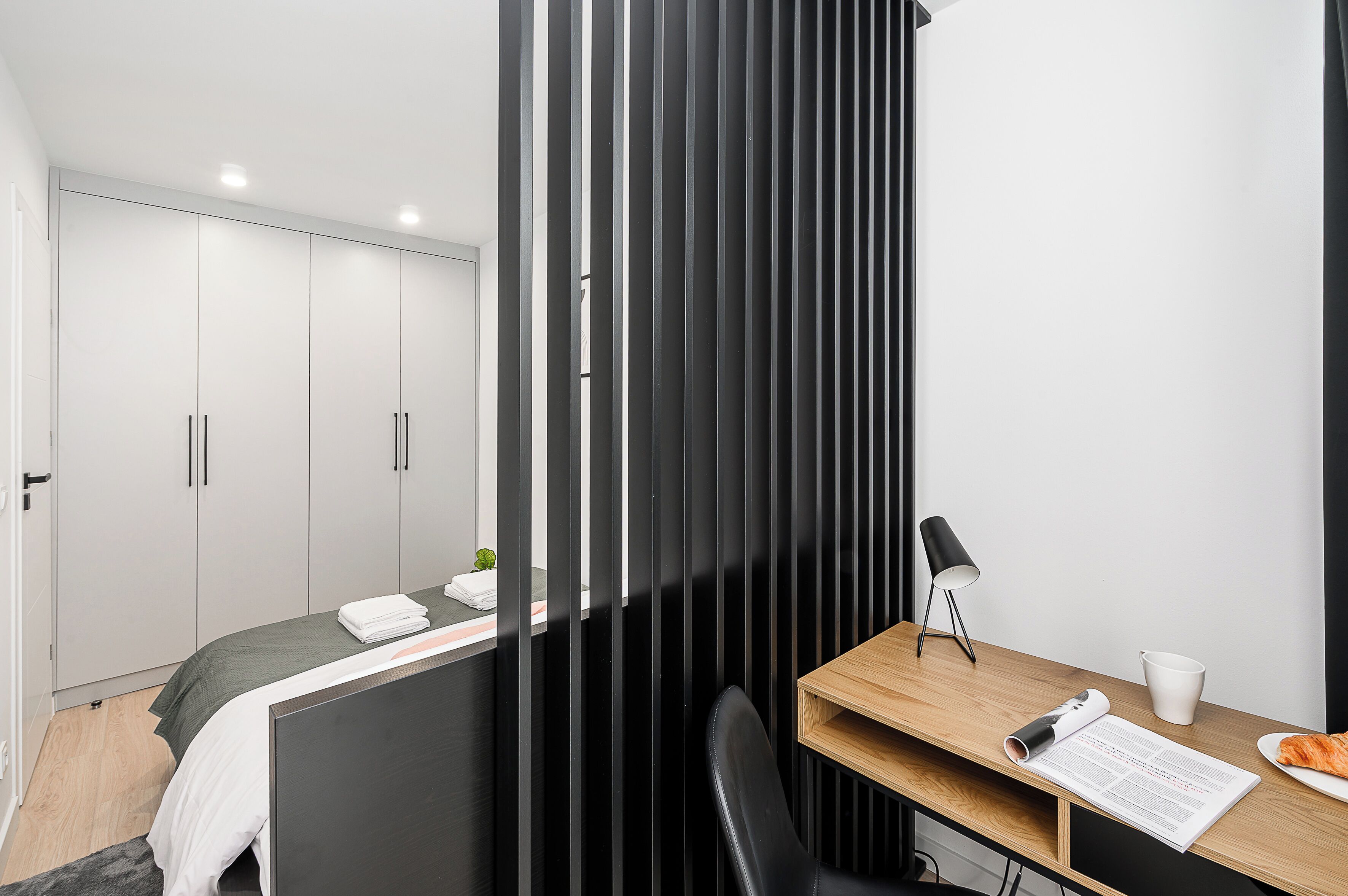 A modern bedroom with a bed, a desk with a lamp, and a chair.