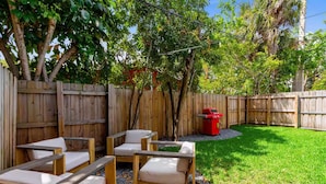 Patio trasero con cerca de madera, una parrilla y mobiliario exterior.