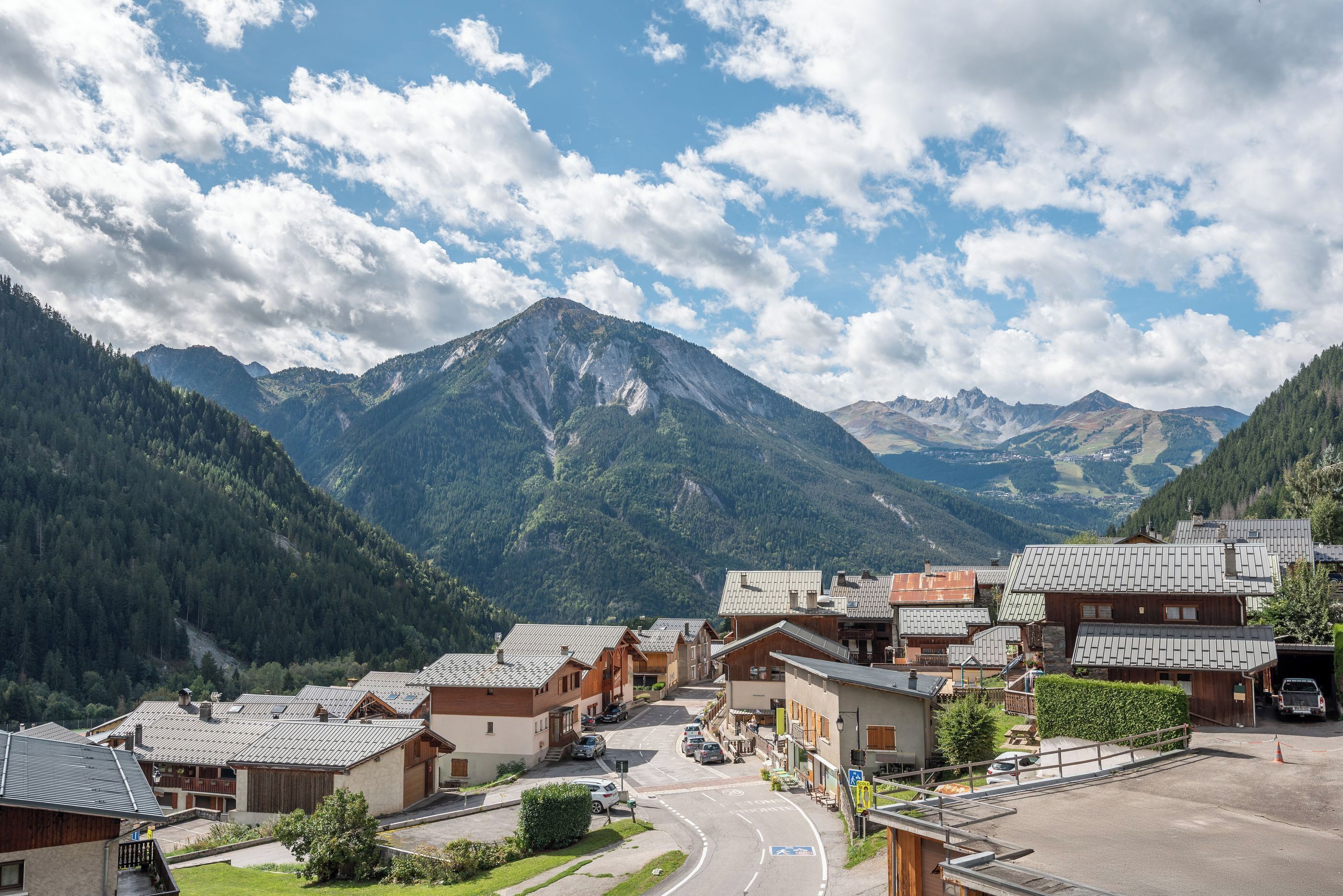 A mountain village with traditional wooden houses, a main road, and a mountain backdrop.