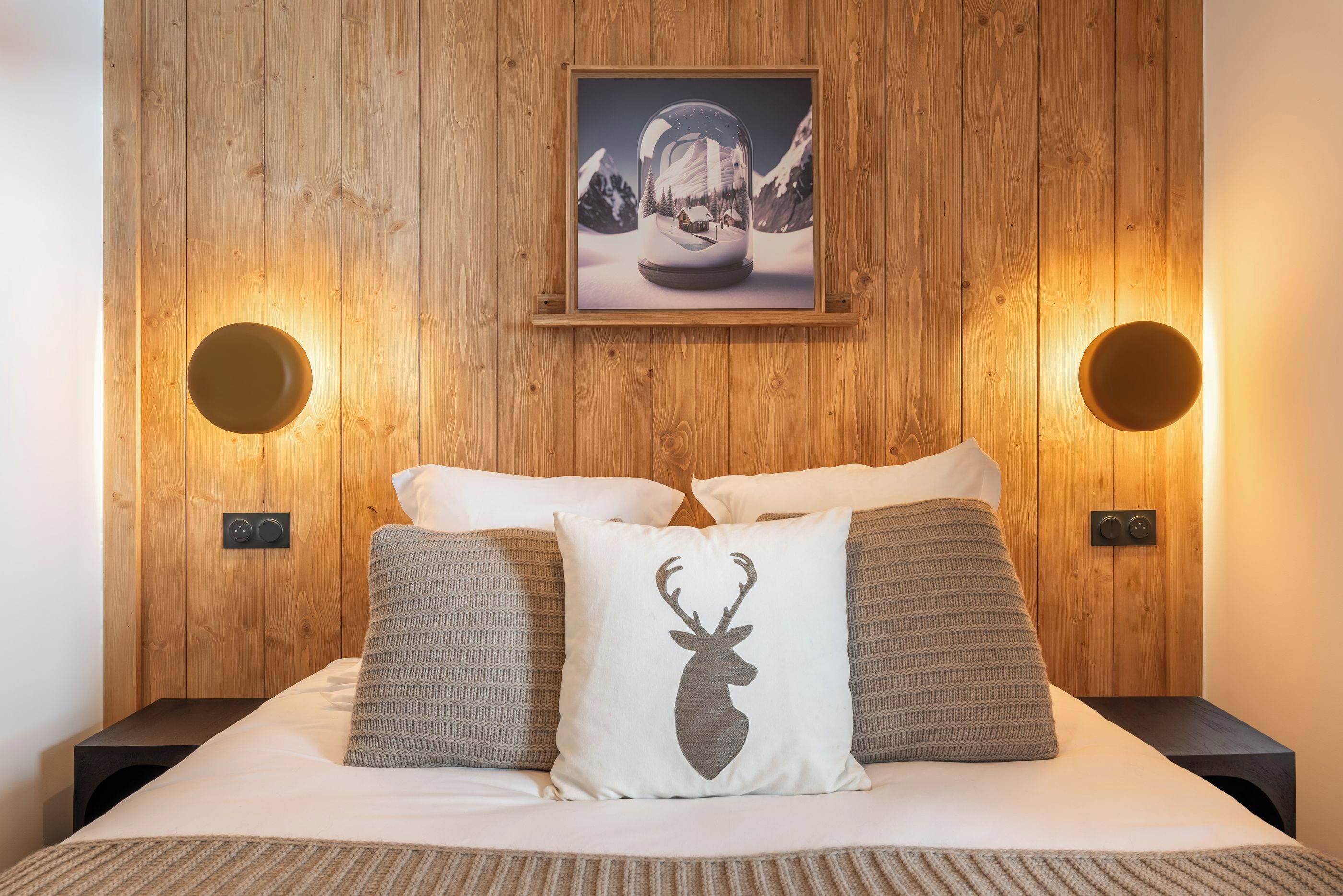 Un dormitorio con cabecera de madera, un cuadro enmarcado sobre la cama y dos lámparas fijadas a la pared.