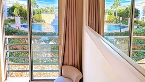 Een kamer met een grote schuifdeur naar een zwembadgedeelte, een fauteuil en uitzicht op een wooncomplex.