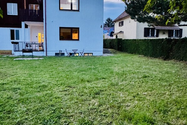 Ein modernes, zweistöckiges Gebäude mit gepflegtem Rasen, Außenbestuhlung und einem sichtbaren Balkon.