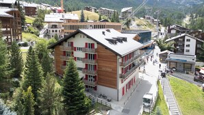 A multi-story building with balconies, a ski lift in the background, and a mountainous landscape. - Alpin Apartment bei der Bergbahn (Zermatt)