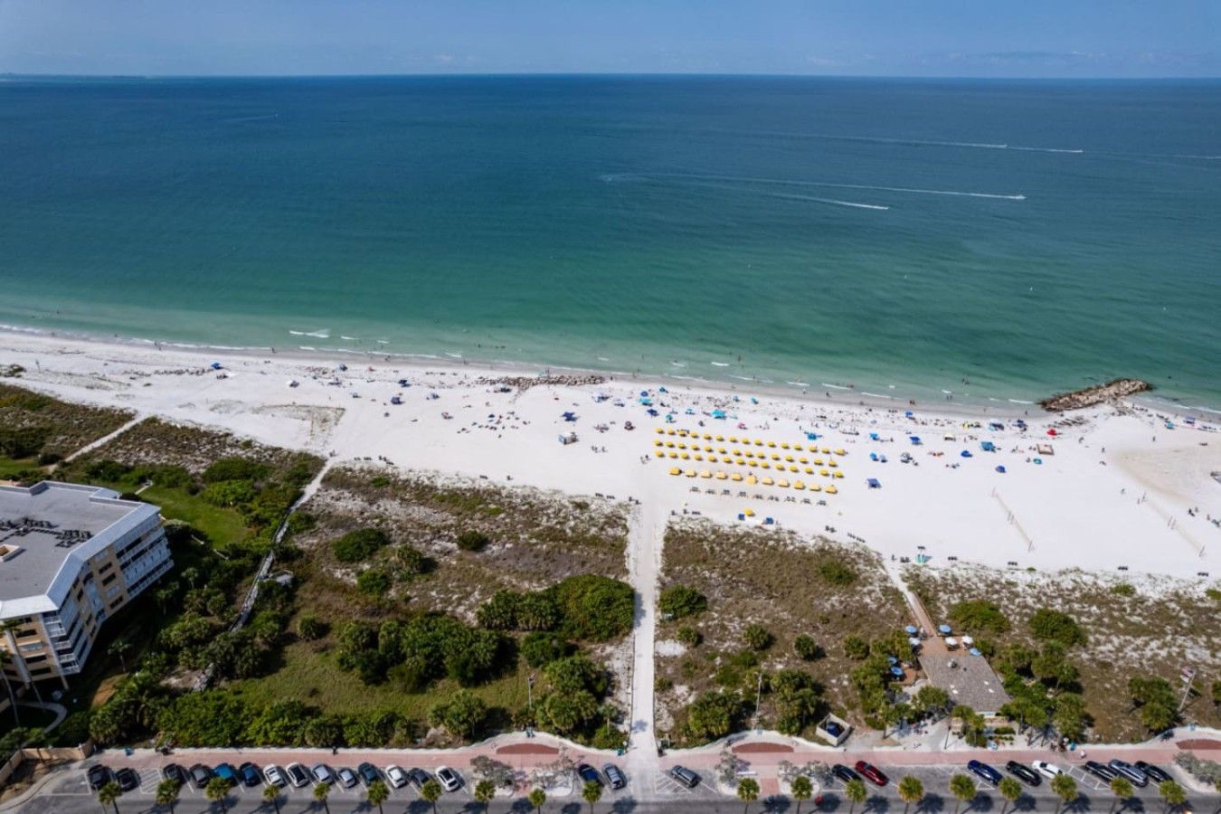 Vue aérienne d’une plage avec des rangées de parasols et un parking rempli de voitures.