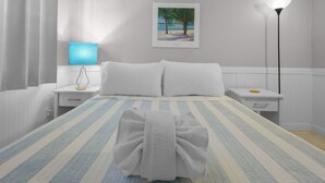 A hotel room with a bed, a nightstand, a lamp, and a painting on the wall. - Beachside Getaway: 2-Bed Condo with Pool, Walk to St. Pete Sand (St. Pete Beach/Tierra Verde)