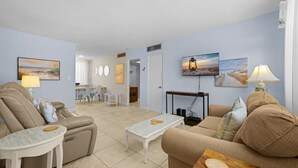 A living room with a sofa, armchair, coffee table, and a dining area with chairs and a table. - Beachside Getaway: 2-Bed Condo with Pool, Walk to St. Pete Sand (St. Pete Beach/Tierra Verde)