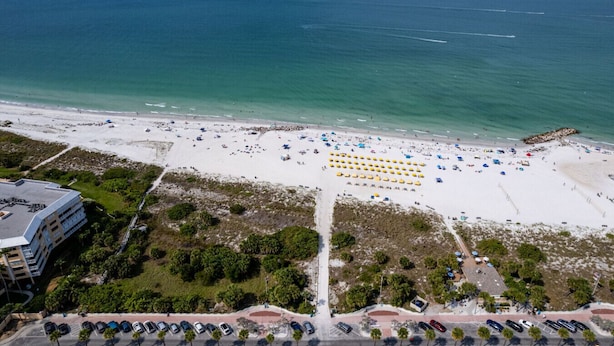 An aerial view of a beach with rows of umbrellas, a parking lot, and a building in the foreground. - Beachside Getaway: 2-Bed Condo with Pool, Walk to St. Pete Sand (St. Pete Beach/Tierra Verde)