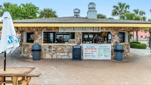 A beachfront restaurant with a stone facade, outdoor seating, and a menu board. - Beachside Getaway: 2-Bed Condo with Pool, Walk to St. Pete Sand (St. Pete Beach/Tierra Verde)