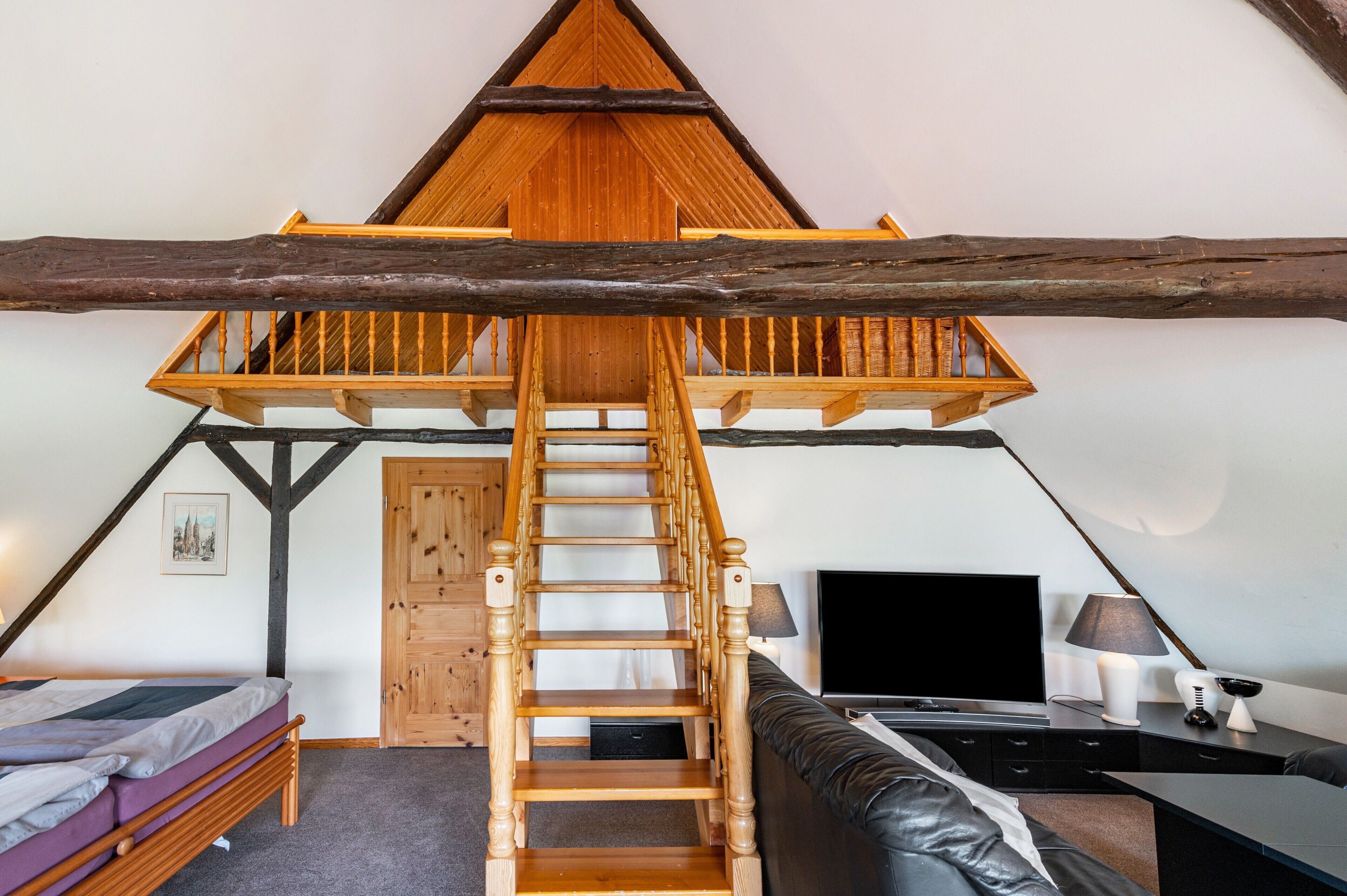 Une chambre située en mezzanine, accessible par une échelle en bois menant à un plafond en pente, avec un lit, un bureau et un téléviseur.