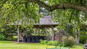 A covered outdoor seating area with a swing chair, a barbecue grill, and a wooden bench. - Cottage 'Haus Am See' with Private Terrace, Private Garden and Wi-Fi (Witzin)
