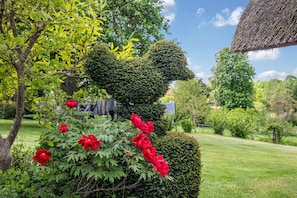 Un jardín con un topiario con forma de oso, abundante vegetación y flores rojas.