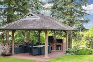 Un gazebo con forno in mattoni, arredi da esterno e un muro in pietra.