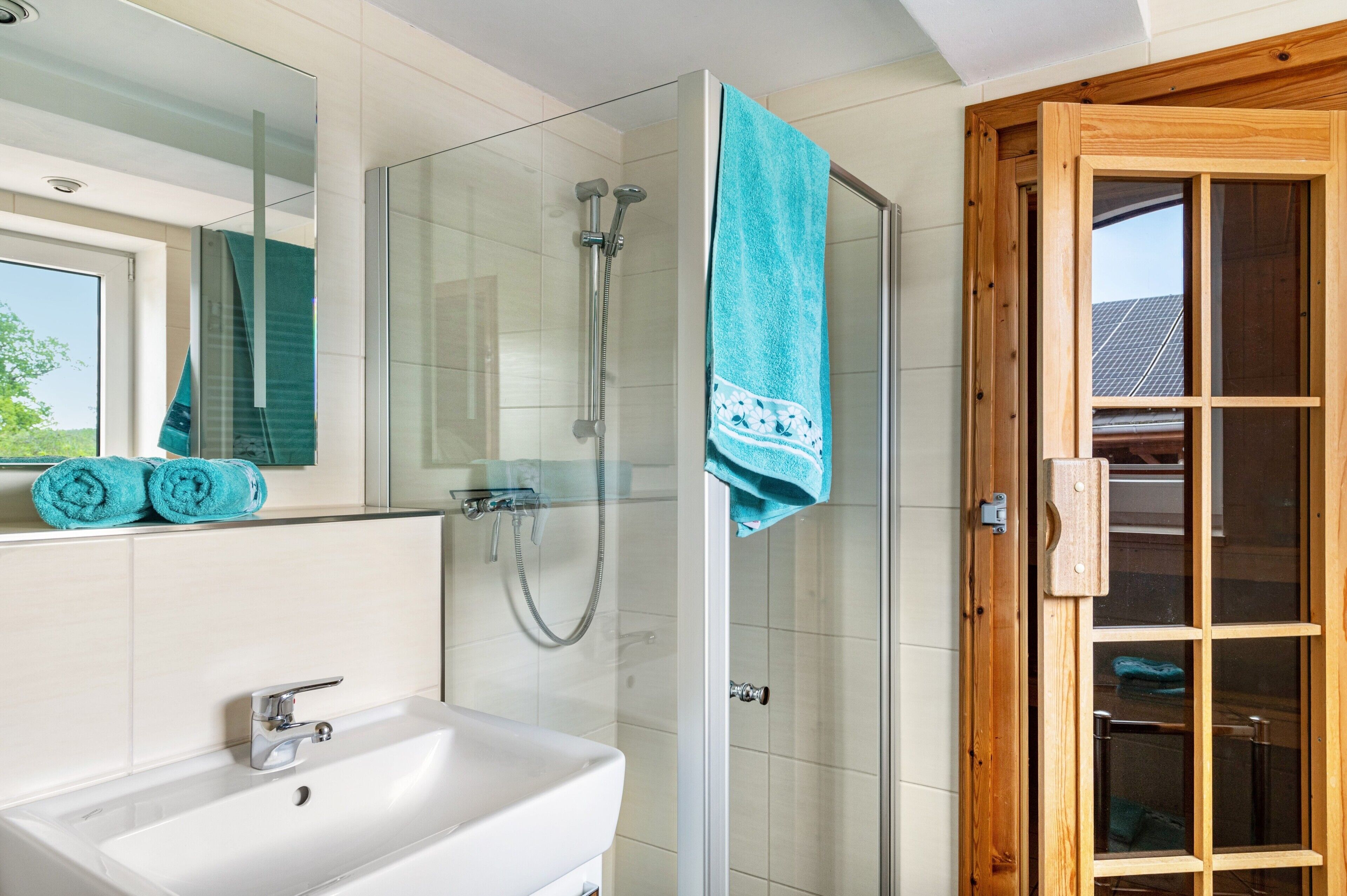 Une salle de bain avec une douche à parois de verre, un lavabo blanc et une porte en bois dotée de panneaux de verre.