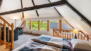 A cozy attic bedroom with a sloped ceiling, a bed, a seating area, and large windows offering a view of greenery. - Cottage 'Haus Am See' with Private Terrace, Private Garden and Wi-Fi (Witzin)