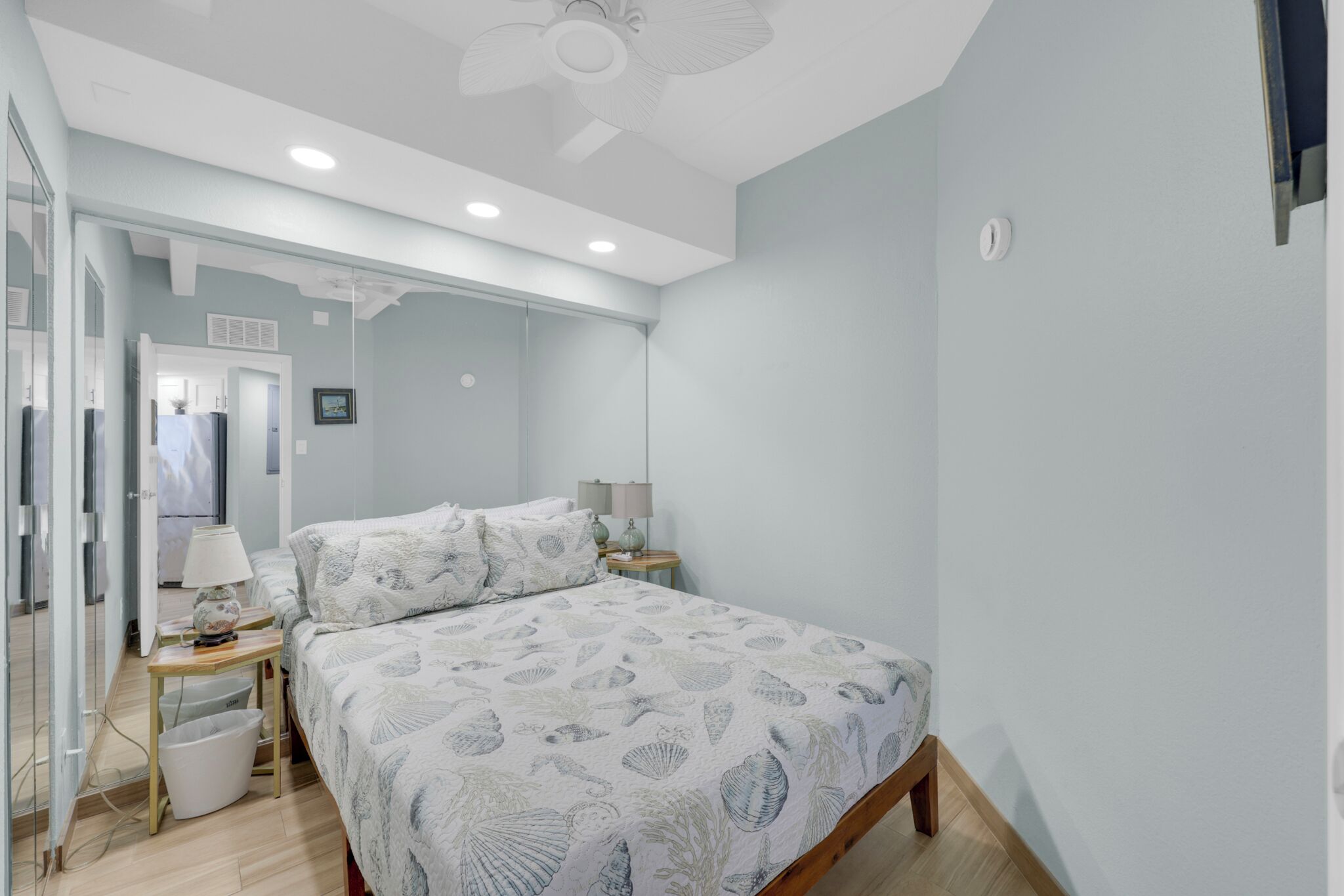 Une chambre à coucher avec un lit, des tables de chevet, un ventilateur de plafond et une fenêtre.