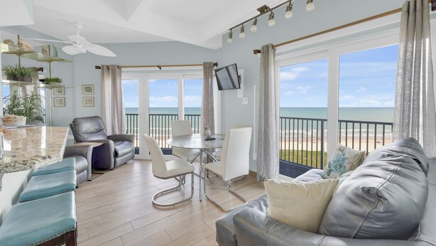 Ein großzügiger Wohnbereich mit Balkon und Blick auf den Strand, inklusive Deckenventilator, Fernseher und Esstisch.