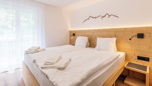 A modern bedroom with a wooden headboard, a bed with white linens, a bedside table, and a wall-mounted light fixture. - Alpin Bijou bei der Bergbahn (Zermatt)
