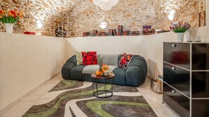 Ein Wohnzimmer mit Steindecke, einem grünen Sofa, einem kleinen runden Tisch mit Obst und einem modernen Schrank.
