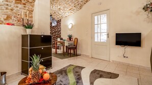 Ein Zimmer mit Steindecke, einem an der Wand montierten Flachbildfernseher, einem Essbereich mit Tisch und Stühlen sowie einem kleinen Tisch mit Früchten.