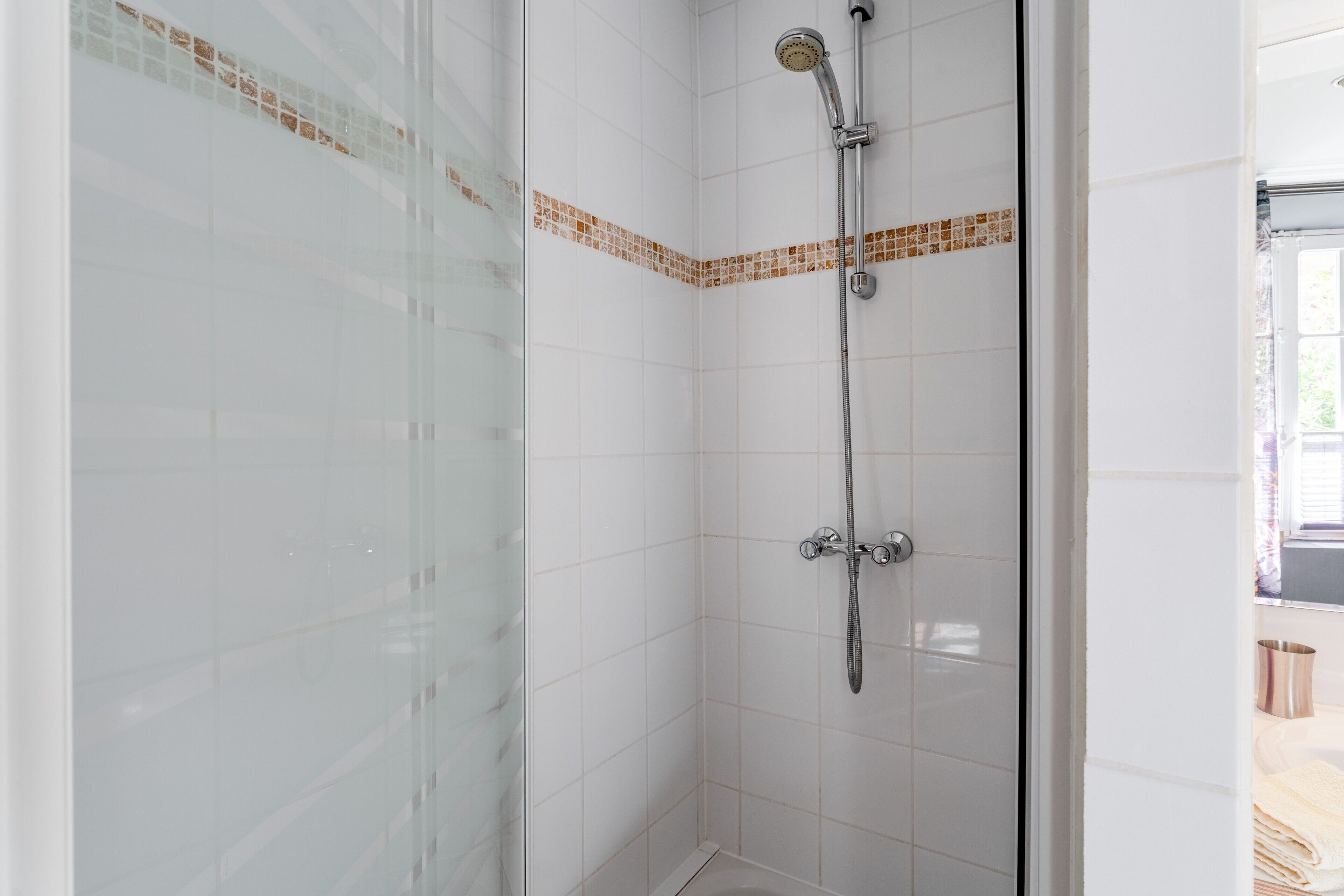 A shower with a glass door, white tiled walls, and a corner tile accent.