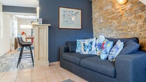 A living room with a stone wall, a sofa with patterned cushions, a framed artwork, and a pendant light. - Gite Bleu - Paradise of Provence (Le Pin)
