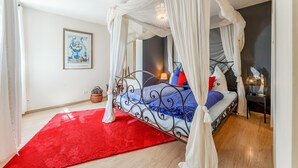 A bedroom with a four-poster bed, a red rug, a framed picture on the wall, and a bedside table with a lamp. - Gite Bleu - Paradise of Provence (Le Pin)