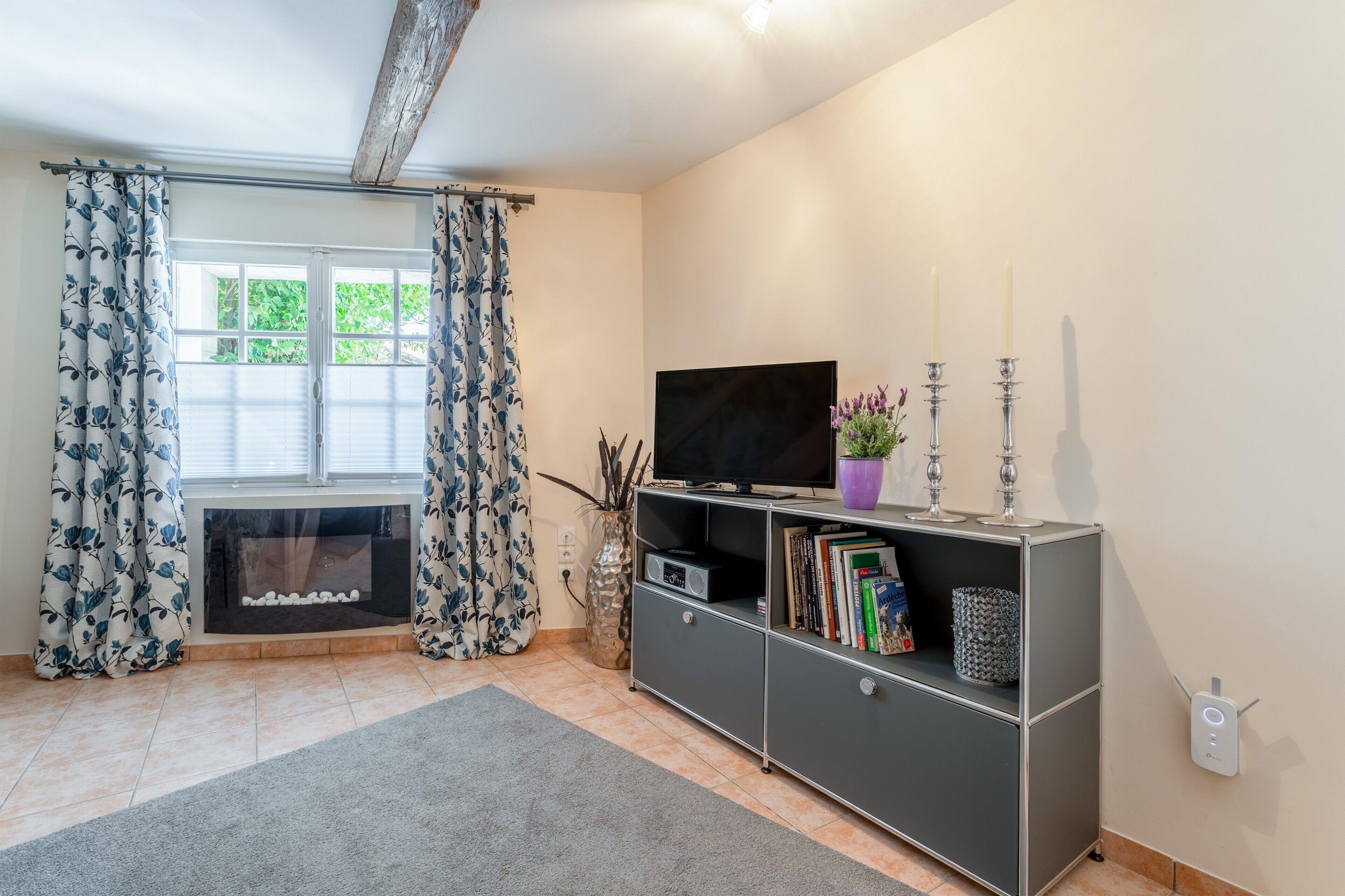 A living room with a fireplace, a television, a bookshelf, and a window with curtains.