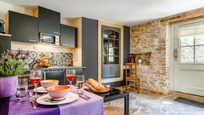 Une cuisine moderne avec des meubles de couleur sombre, un four à micro-ondes encastré et un coin repas agrémenté d’une nappe violette.