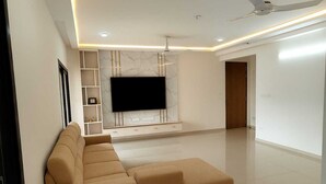 Ein modernes Wohnzimmer mit einem beigefarbenen Ecksofa, einem Flachbildfernseher an einer Marmorwand und einem Deckenventilator.