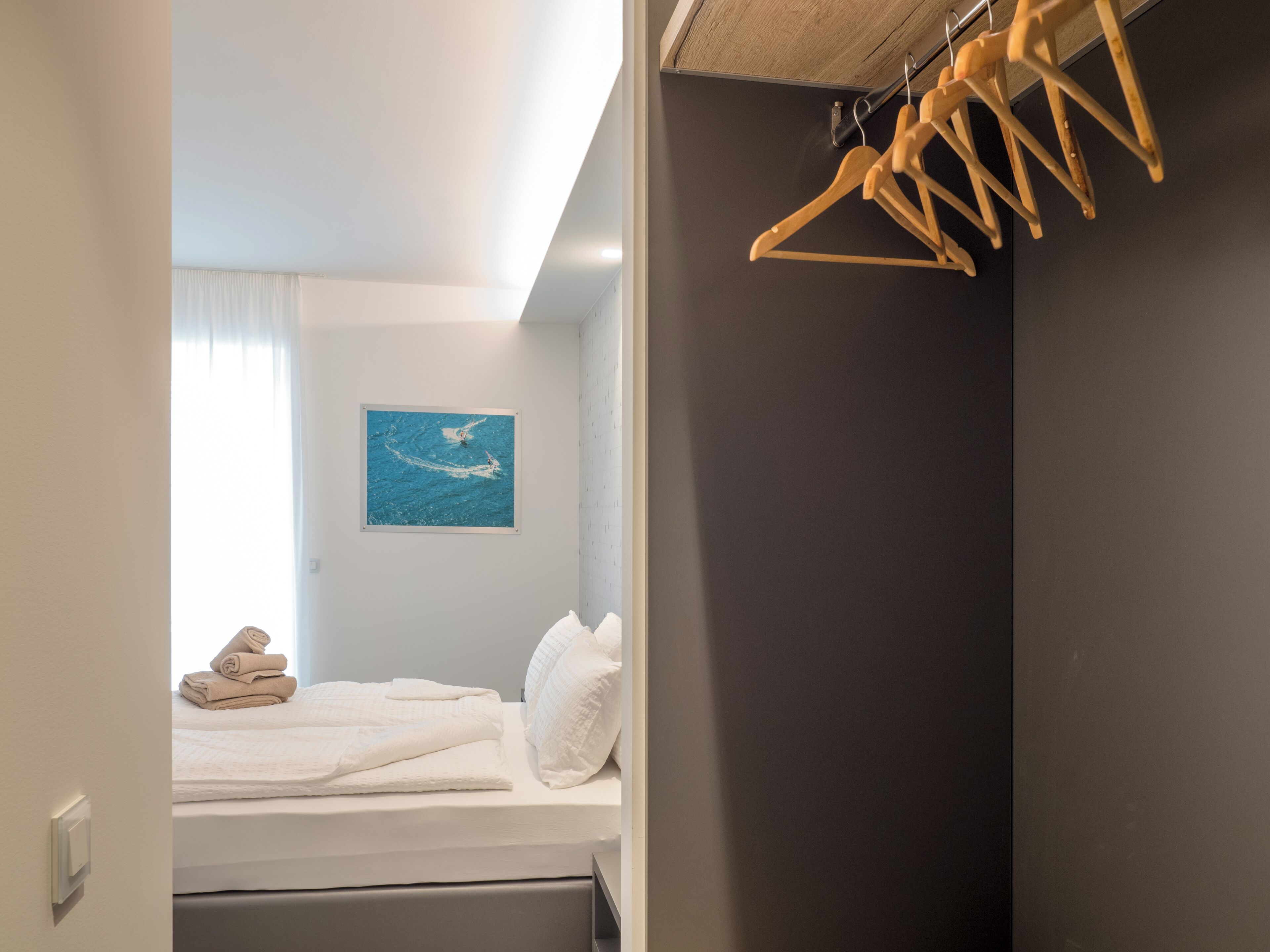 A hotel room with a bed, a wooden hanger rack, and a painting of a seascape.