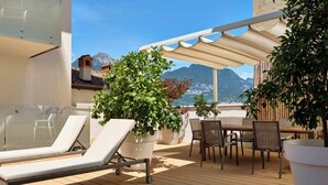 Eine Terrasse mit Liegestühlen, einem Tisch und Topfpflanzen mit Blick auf eine Berglandschaft.