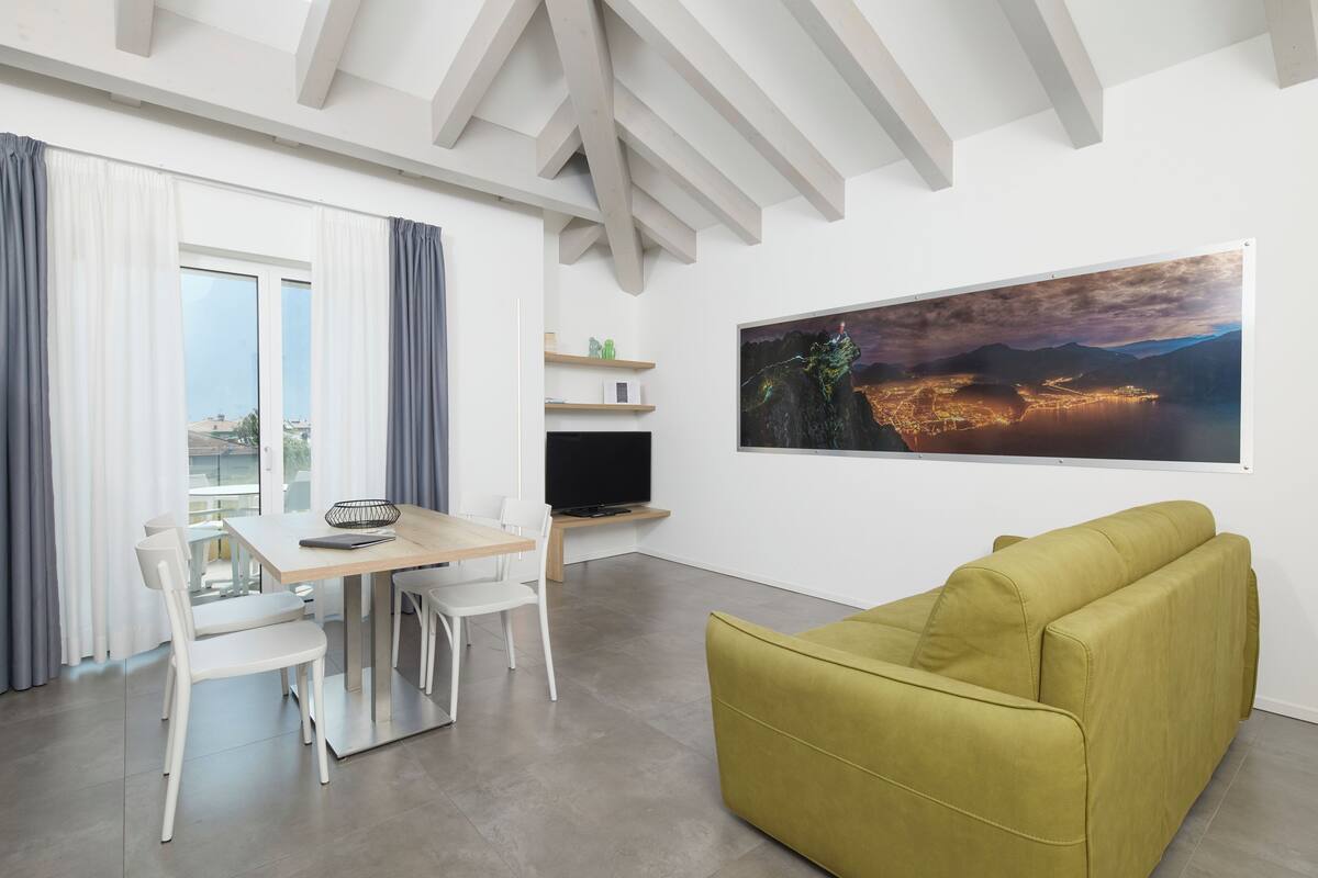 A modern living room with a dining area, a sofa, a TV, and a large cityscape painting on the wall.