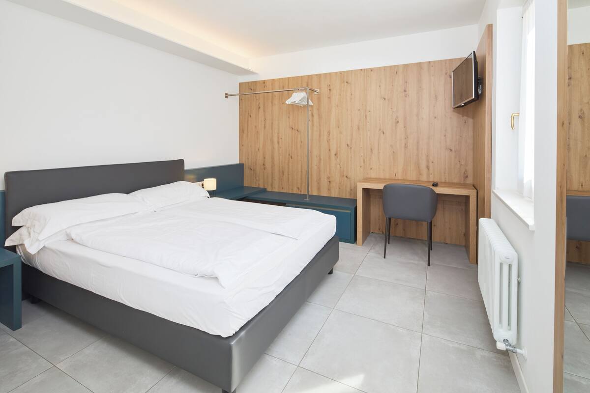 A modern bedroom with a large bed, a desk, and a TV mounted on the wall.