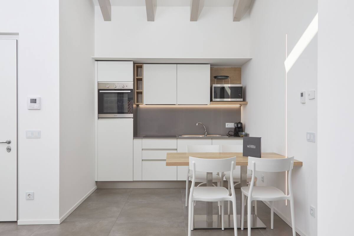 A modern kitchen with white cabinetry, a wooden countertop, and two white chairs.