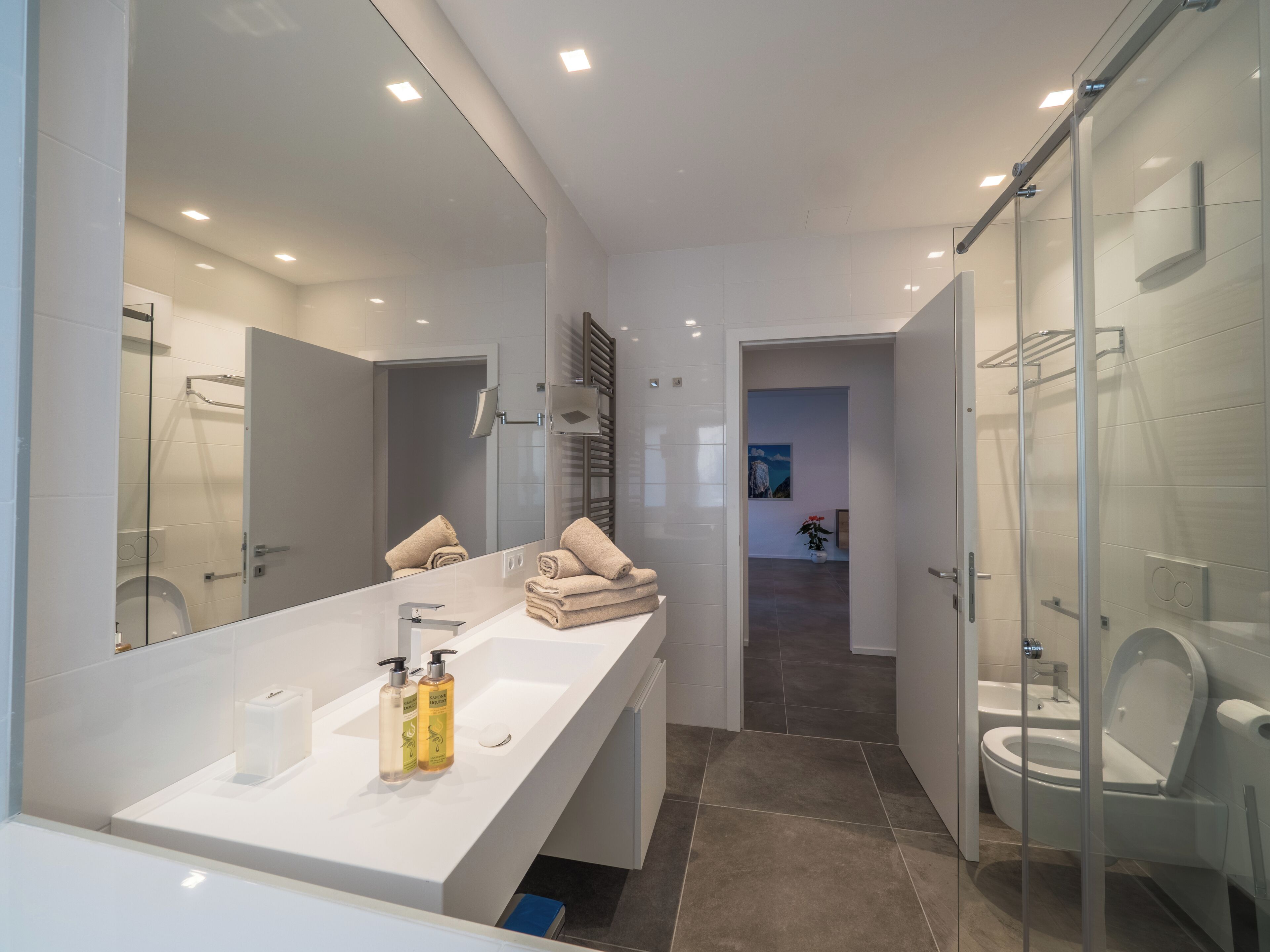 Ein modernes Badezimmer mit einem großen Spiegel, einem weißen Waschbecken und einer Duschkabine aus Glas.