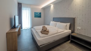 Ein modernes Hotelzimmer mit einem großen Bett, einem Flachbildfernseher auf einem Holzboden, einem Nachttisch und einer Wandleuchte.