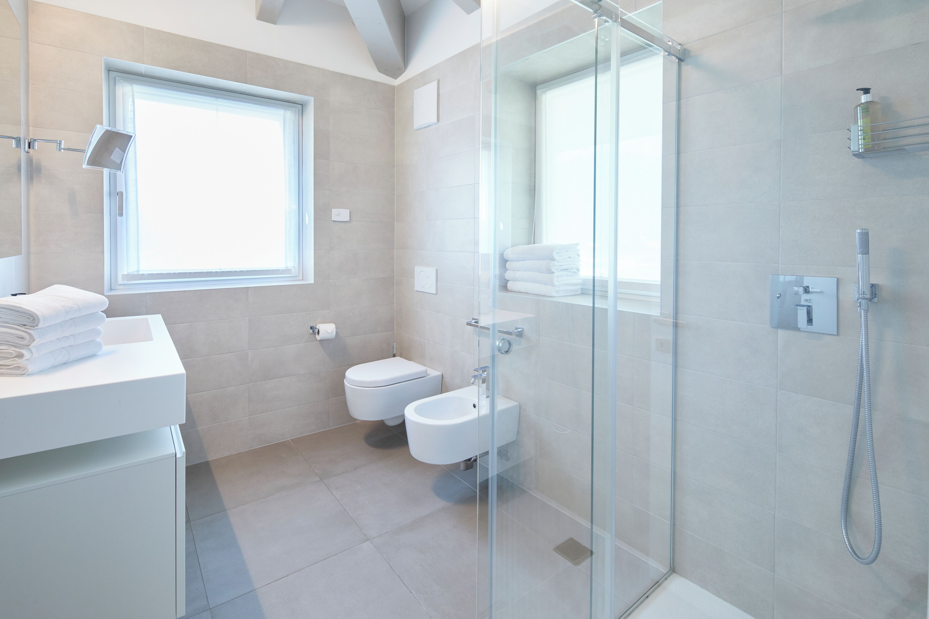 A modern bathroom with a glass shower enclosure, a toilet, and a bidet.