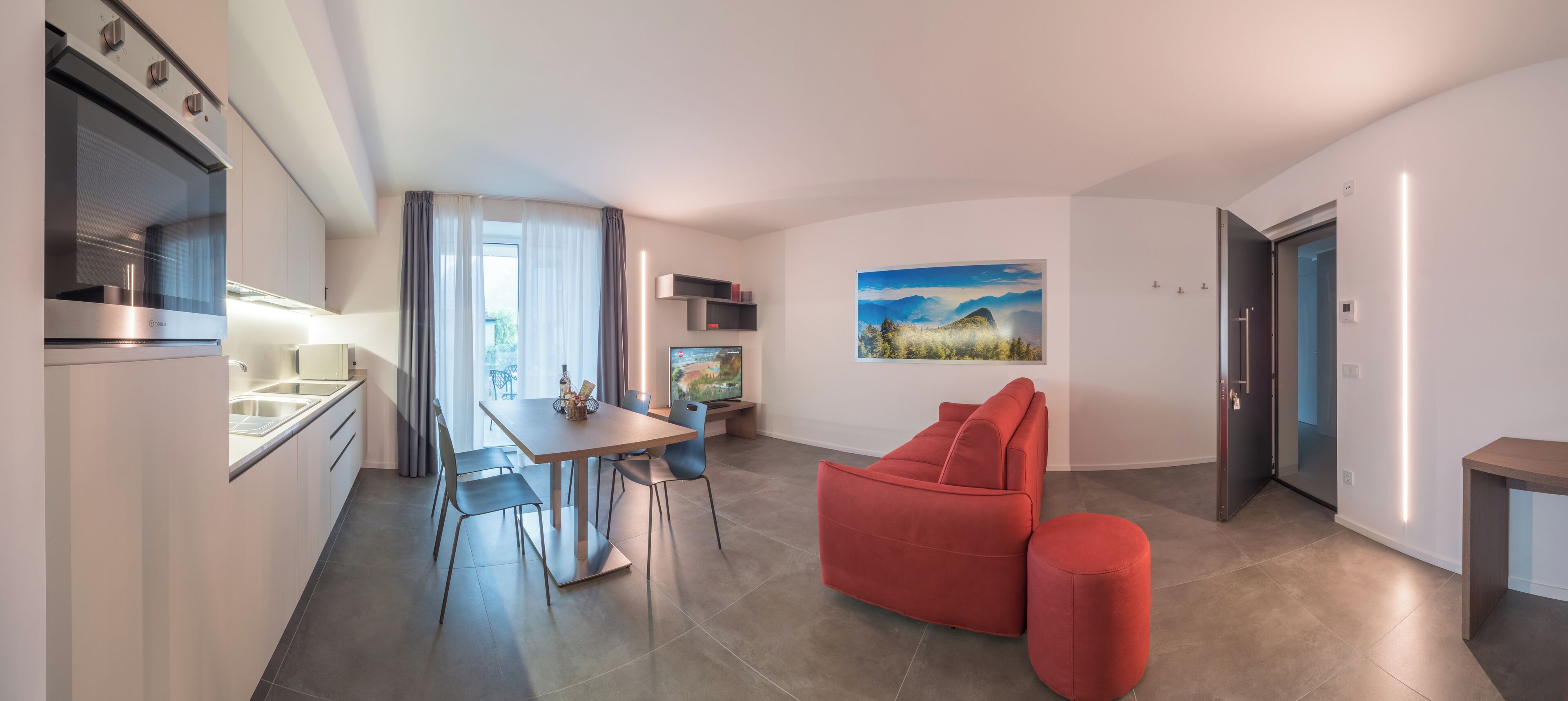 A modern kitchen with a built-in oven, a dining area with a table and chairs, a red sofa, and a painting on the wall.