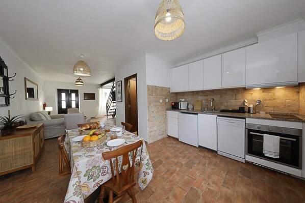 A spacious kitchen with white cabinets, a dining table set with plates and fruits, and a staircase leading to another level.